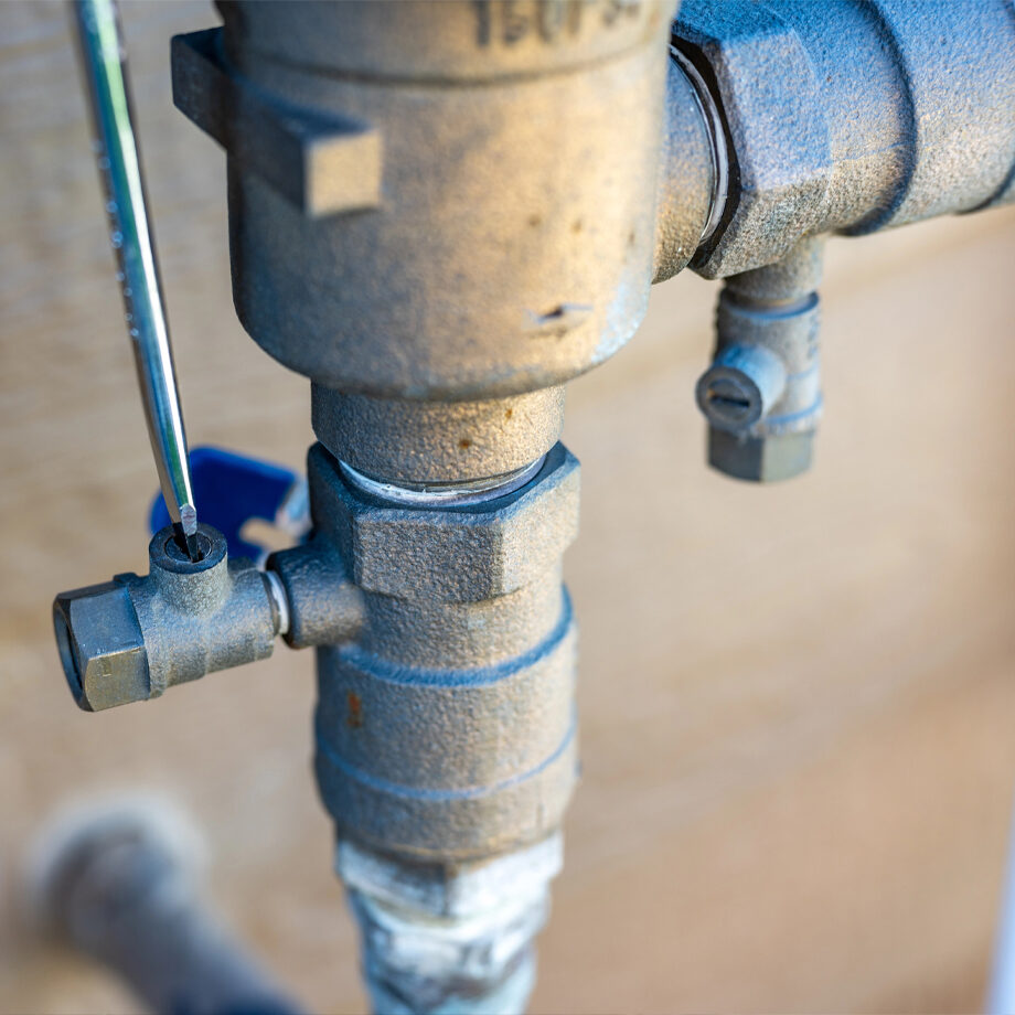 Technician inspecting an outdoor irrigation backflow preventer for testing and repair.